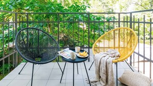 A balcony with two chairs, a table, and a view of lush greenery.