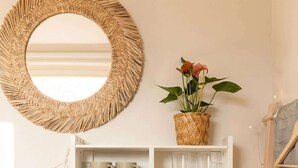 A white desk with shelves holding mugs, plates, and glasses, a woven mirror, a potted plant, and a black speaker. - TurnKey | Angelo Roma Cozy Studio I (Praha 2)