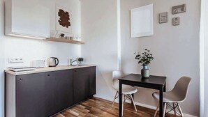 A modern kitchen with dark cabinets, a countertop, and a sink. There is a dining table with two chairs and a vase with flowers.