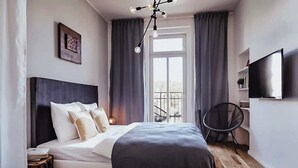 A modern bedroom with a large bed, a TV, and a balcony view.