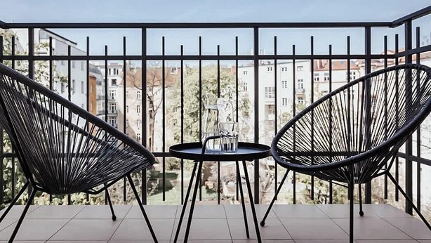 A balcony with two black wire chairs and a small round table with a glass and a bottle.