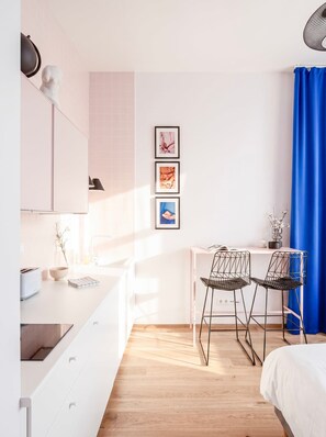 A modern bedroom with a bed, a desk with two chairs, a window with curtains, and a wall with framed pictures. - TurnKey | Florenc Studio by Central Bus Station (Praha 8)
