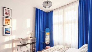 Un dormitorio con una cama, un escritorio con sillas, un espejo y una ventana con cortinas azules.
