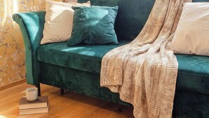 A teal sofa with a patterned throw blanket, a lamp, and a floral wallpaper.