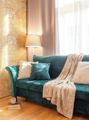 A teal sofa with a patterned throw blanket, a lamp, and a floral wallpaper.