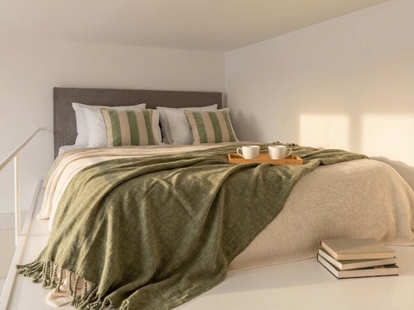 A neatly made bed with pillows, a green throw blanket, and a tray with two cups.