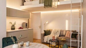 A compact living space with a loft bed, kitchenette, sofa, and a small round table.