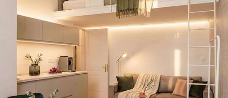 A compact living space with a loft bed, kitchenette, sofa, and a small round table.