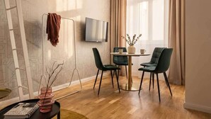 A modern living room with a TV, a dining table with chairs, a vase with branches, and a ladder against the wall.