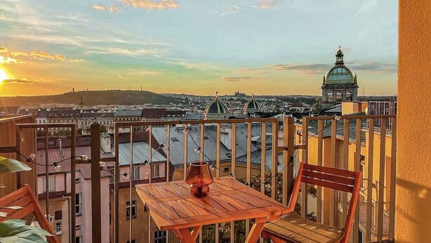 A balcony with a table and chairs, overlooking a cityscape with buildings and a dome structure. - TurnKey | Angelo Roma Studio - Premium View (Praha 2)