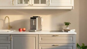 A kitchen with white cabinets, a stainless steel coffee maker, a gold faucet, and a potted plant. - TurnKey | Angelo Roma Studio III (Praha 2)