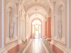 A grand hallway with classical architecture, including columns and statues, leading to a bright doorway.
