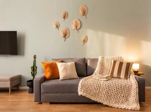 A living room with a grey sofa, a knitted throw blanket, and a cactus plant.