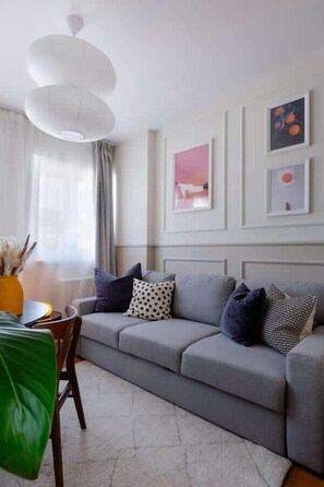 A modern living room with a grey sofa, a white ceiling light fixture, and framed artwork on the wall.