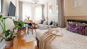 A modern bedroom with a bed, a sofa, a dining table, and a TV.