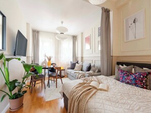 A modern bedroom with a bed, a sofa, a dining table, and a TV. - TurnKey | Vineyard Terrace Apartment (Praha 2)