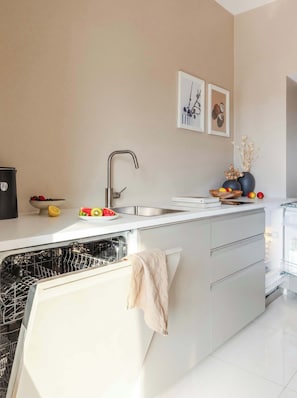 A modern kitchen with a built-in dishwasher, a stainless steel sink, and a countertop with fruits and a bowl. - TurnKey | Vineyard Terrace Apartment (Praha 2)