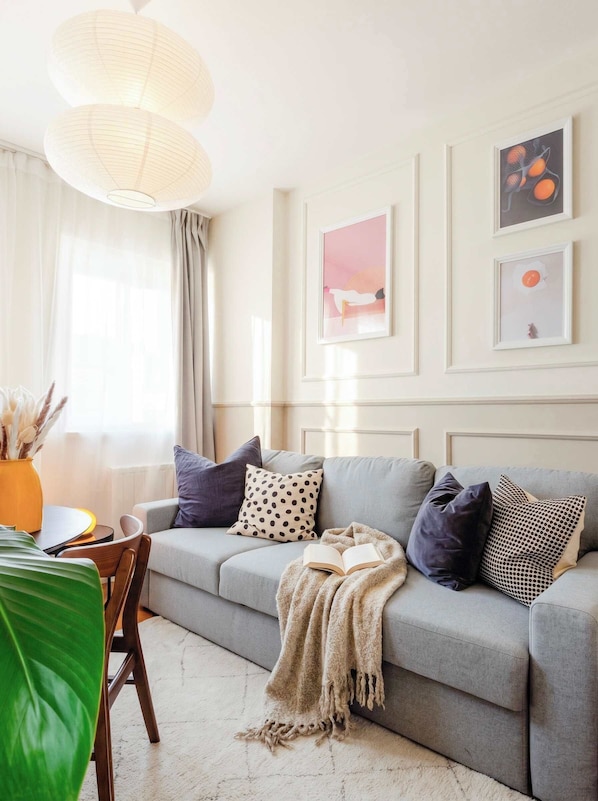 A modern living room with a grey sofa, a large window with sheer curtains, and artwork on the walls. - TurnKey | Vineyard Terrace Apartment (Praha 2)