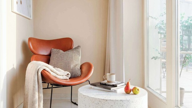 A modern living room with a leather armchair, a round coffee table with books and fruit, and a large window with a view.