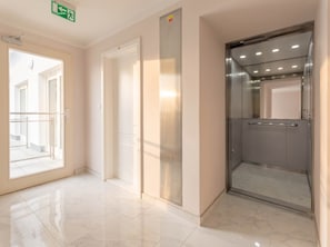 A clean, modern elevator with a metallic finish, a glass door, and a handrail. - TurnKey | Vineyard Terrace Apartment (Praha 2)