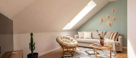 A loft-style room with a sloped ceiling, a sofa, a round chair, a coffee table, a cactus plant, and a patterned rug.