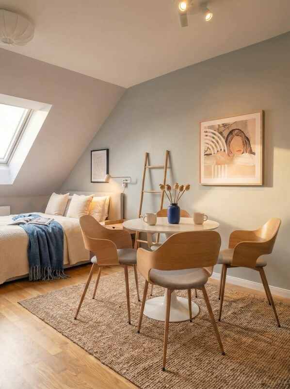 Una habitación acogedora con una cama, una mesa redonda con sillas, una escalera y una obra de arte enmarcada en la pared.