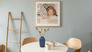 A round table with chairs, a vase with dried flowers, and a framed artwork on the wall.