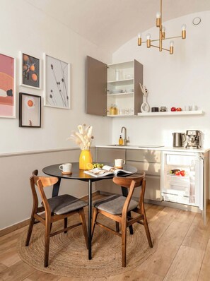 A modern kitchen with a dining area, featuring a round table with chairs, a coffee machine, and a refrigerator.