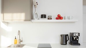 Cocina moderna con encimera blanca, cafetera, hervidor y estante con manzanas y frascos.
