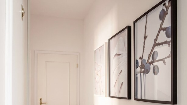 Un pasillo con una puerta blanca, paredes color beige y tres obras de arte enmarcadas en la pared.