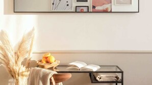 Un dormitorio con cama, una mesita de noche con un libro y un frutero, una silla con una manta, una lámpara de pared y obras de arte enmarcadas.