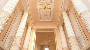Una imponente escalera con columnas ornamentales y una alfombra roja que conduce a una puerta en la parte superior.