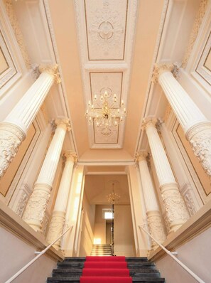 A grand staircase with ornate columns and a red carpet leading to a door at the top.