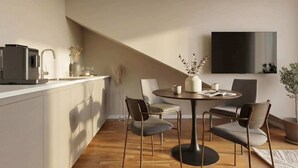 Une cuisine moderne équipée d’une machine à café intégrée, un coin repas avec une table ronde et quatre chaises, et un téléviseur à écran plat fixé au mur.