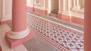 A grand hallway with a pink and white color scheme, featuring a large column, a patterned floor, and classical architectural details.