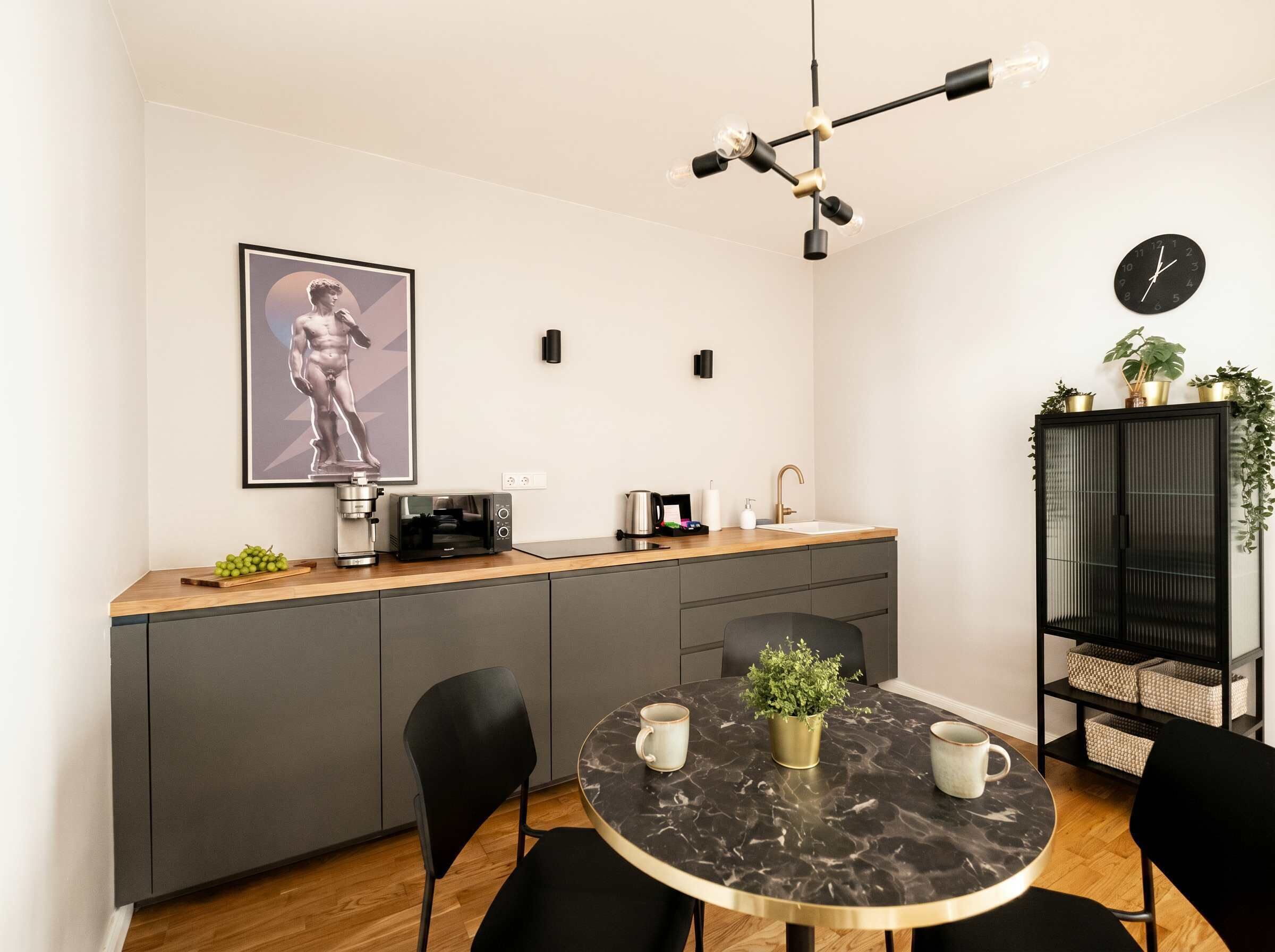 A modern kitchen with a marble dining table, black chairs, a coffee machine, a toaster, and a clock on the wall.