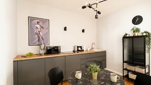A modern kitchen with a marble dining table, black chairs, a coffee machine, a toaster, and a clock on the wall.
