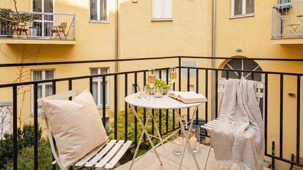 A balcony with a white chair, a small table with a book and candles, and a blanket draped over a chair.