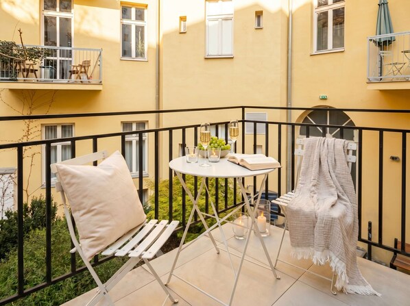 A balcony with a white chair, a small table with a book and candles, and a blanket draped over a chair.