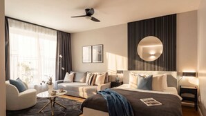A modern hotel room with a bed, two sofas, a coffee table, and a ceiling fan.