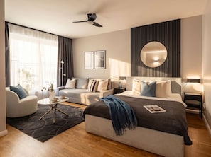 A modern hotel room with a bed, two sofas, a coffee table, and a ceiling fan.