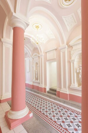 A grand hallway with pink columns, a patterned floor, and classical architectural details.