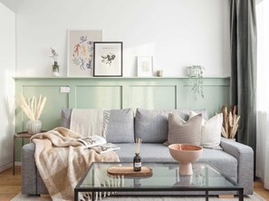 Un salon comprenant un canapé, une table basse en verre et une table d’appoint sur laquelle est posé un vase.