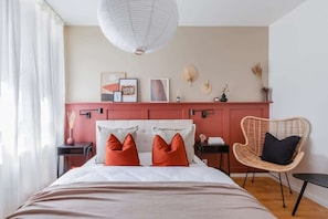 Un dormitorio con cama, una silla, mesita de noche y adornos en la pared.