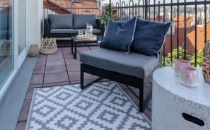 A balcony with a grey sofa, a small table, and a patterned rug. - TurnKey | Letna Park Apartment I – Premium Terrace (Praha 7)