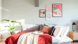 Une chambre moderne avec un canapé-lit gris, une couverture rouge et une plante verte.