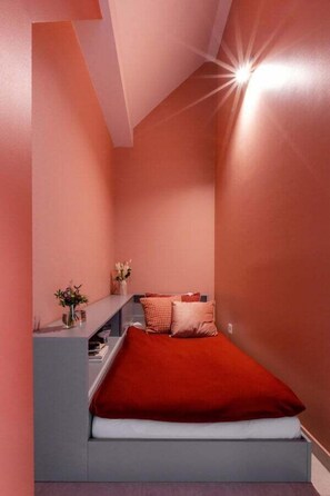 A bedroom with a bed, a nightstand, and a shelf with flowers. - TurnKey | Letna Park Apartment I – Premium Terrace (Praha 7)