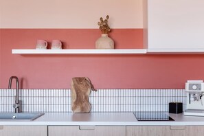 A kitchen with a white countertop, a sink, a coffee machine, and a shelf with decorative items. - TurnKey | Letna Park Apartment I – Premium Terrace (Praha 7)