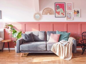 Un salon moderne avec un canapé gris, un plancher en bois et un mur rose.