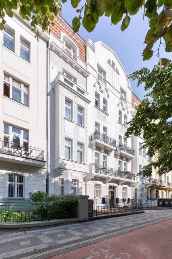 Un immeuble à plusieurs étages de style architectural classique, doté de balcons et d’un toit recouvert de tuiles rouges.